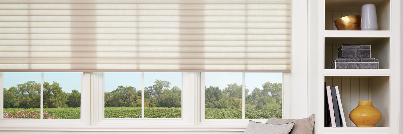 Beige cellular shades over a wide window seat.