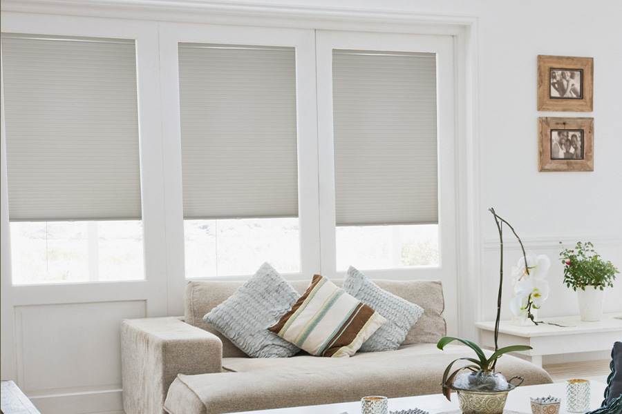 Cellular shades are energy-saving for your living spaces.  Light gray cellular shades on three separate windows in large light wood and beige colored living room.
